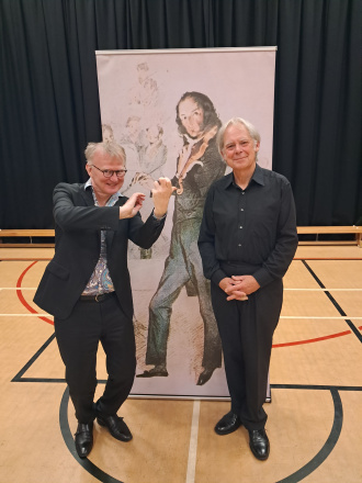 Thomas Bowes posing in front of a picture of Paganini.