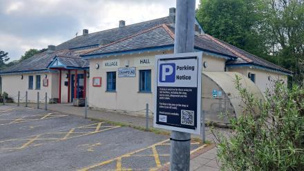 parking notice sign with QR code for quickly paying for parking online. The village hall is seen in the background.