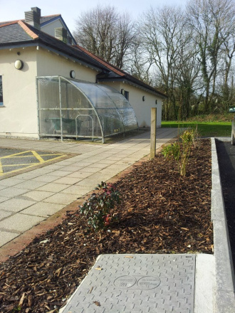 Bark chip covers a shrub area. A manhole is visible in the foreground and a lean-to perspex bike shed in the background.