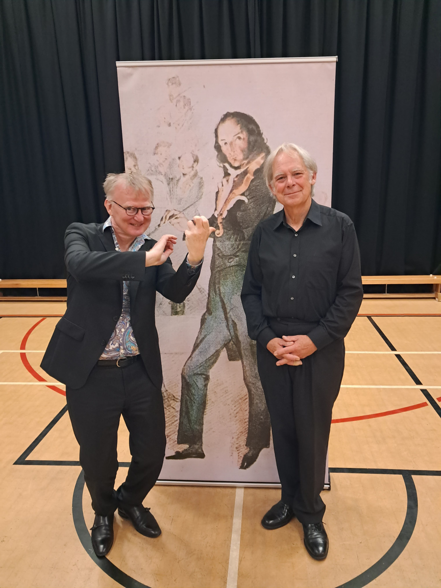 Thomas Bowes posing in front of a picture of Paganini.