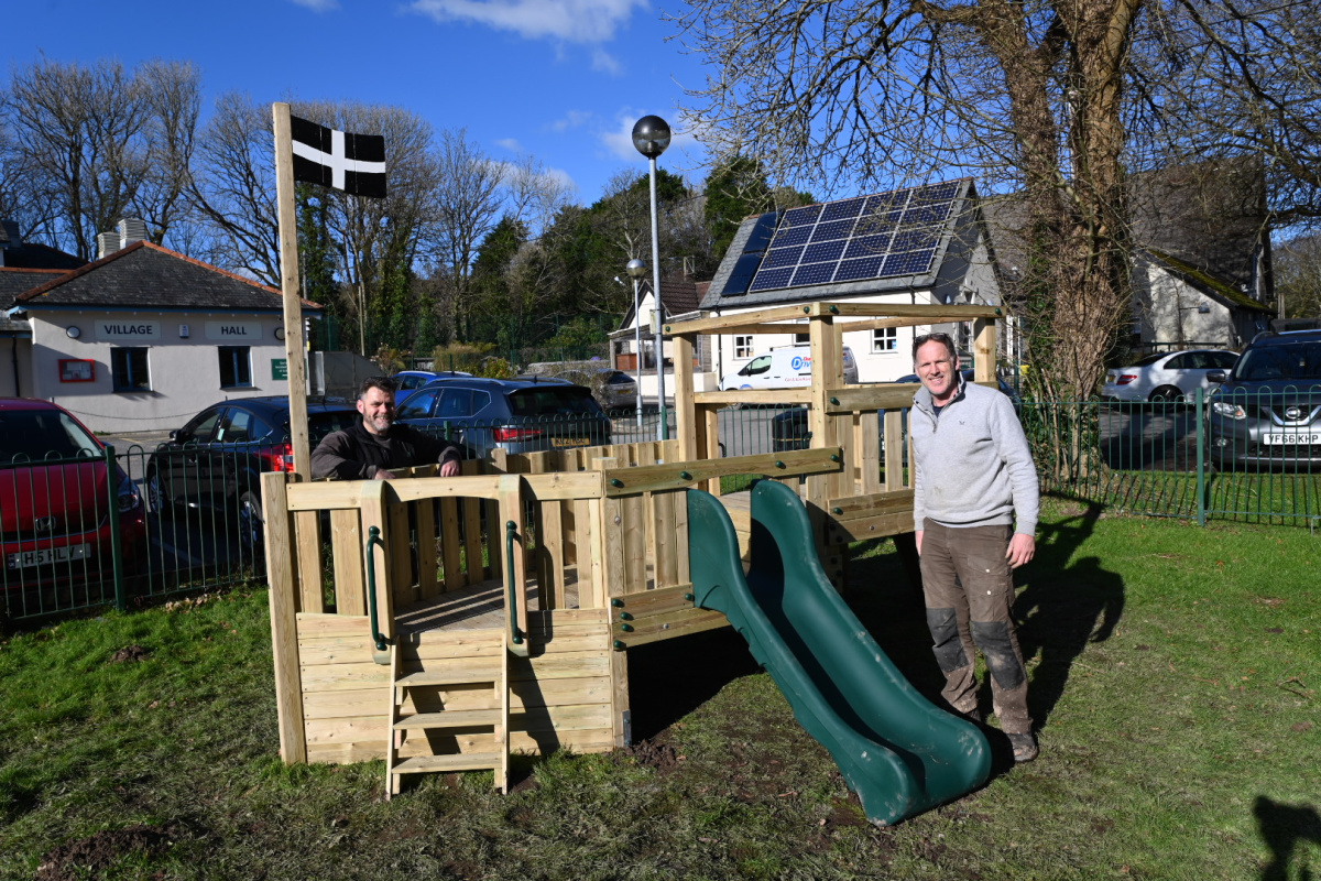 A wooden playground ship with Cornish flag. The two installers are pictured proudly standing next to it.