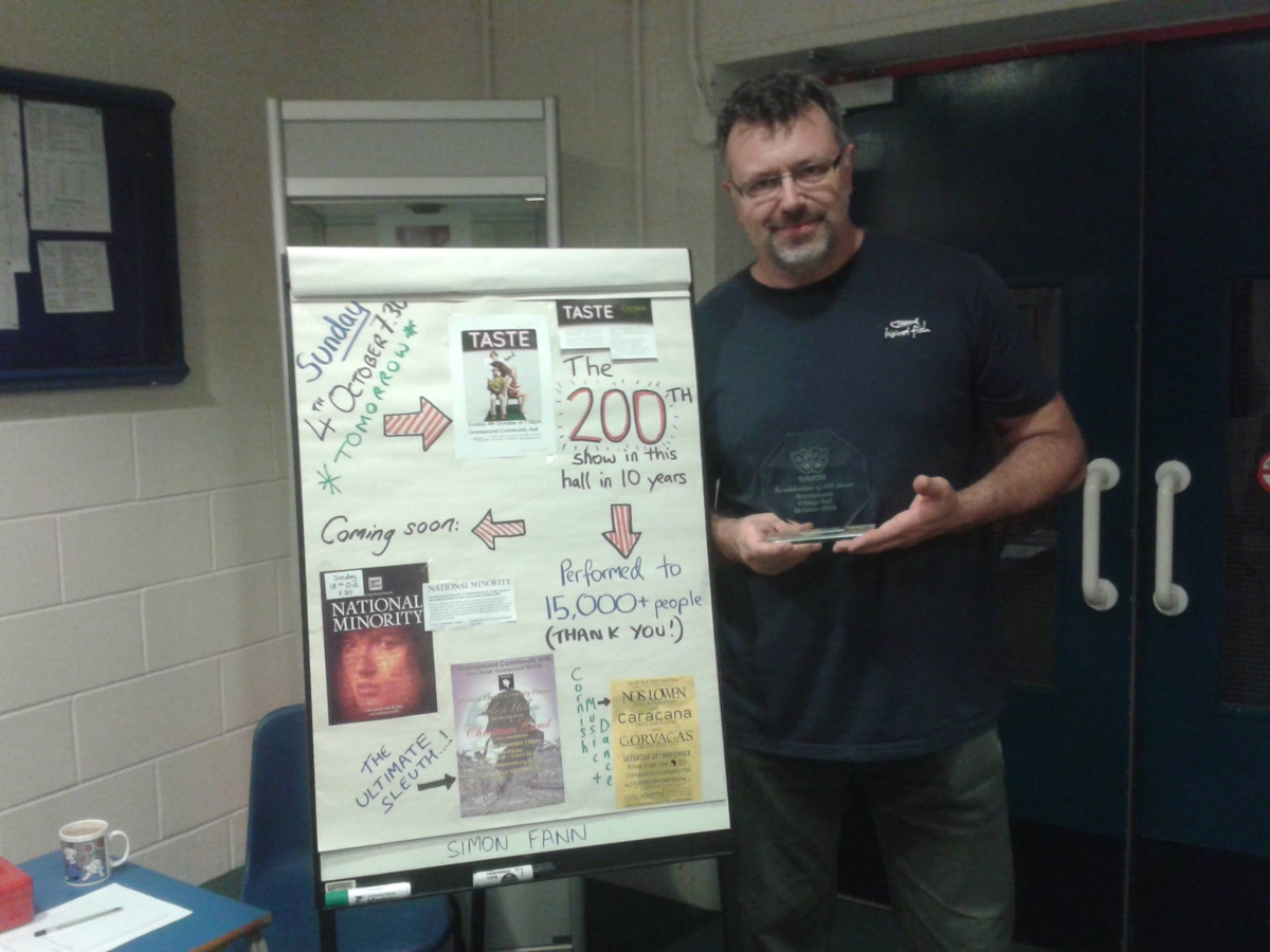 Photo of Simon Fann with a poster explaining the 200 shows of the village hall.